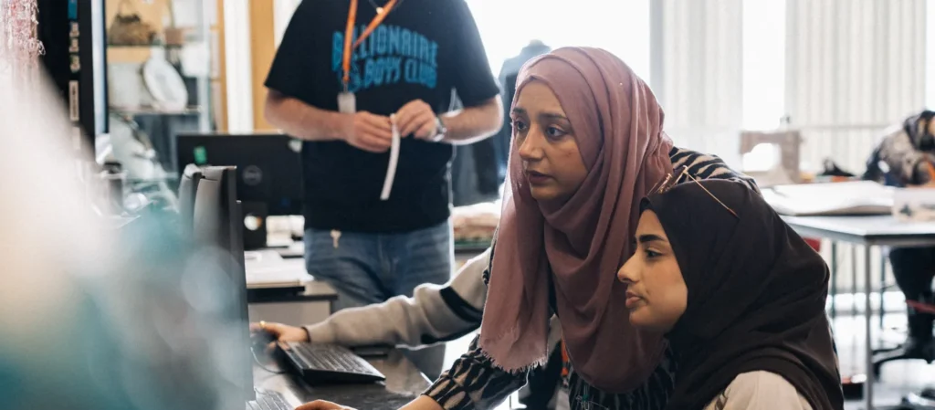 female muslim tutor and student in a computer lab on a computer sat at a desk